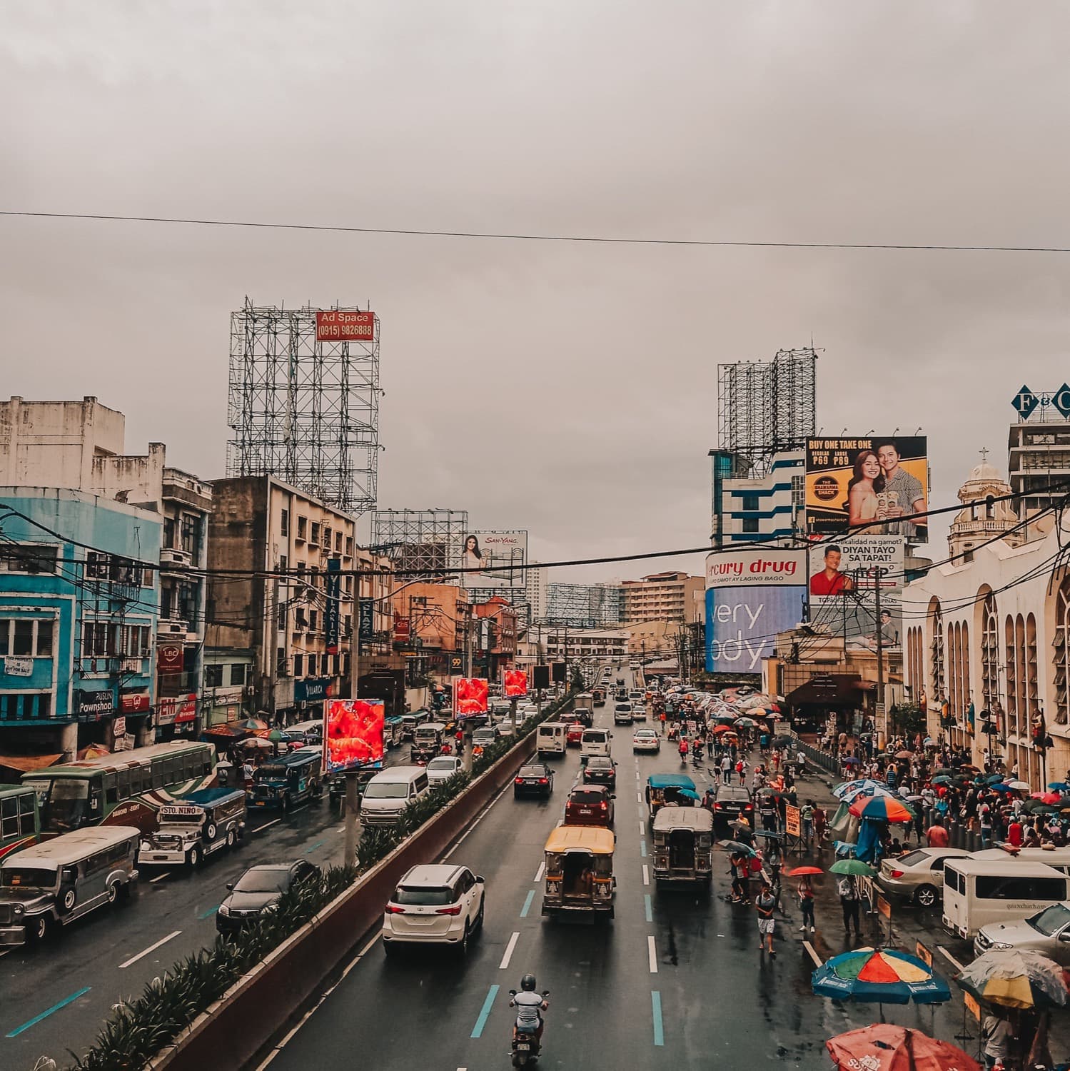 A busy Metro Manila avenue packed with jeepneys, cars, and tricycles beneath a wall of billboards